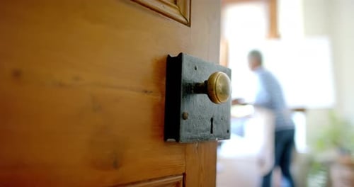 Door over senior biracial woman wearing apron and painting on big canvas at home, slow motion