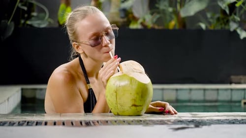 Rich Young Successful Woman Relaxing in Her Pool Villa Drinking Whole Coconut