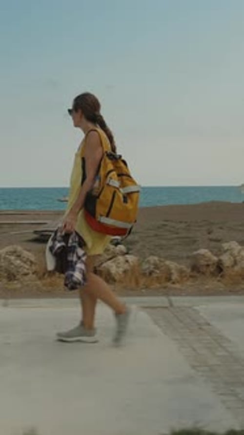 Vertical video. A Woman Walks Along the Seaside Path, Wrapped in a Yellow Towel, With the Ocean and