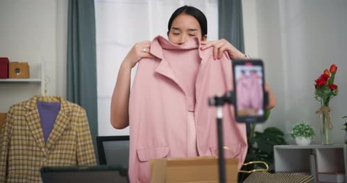 Young woman business owner stand selling clothes while live streaming on mobile phone at home.