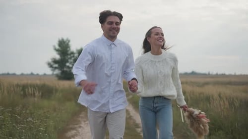 Couple Running Happily Through a Field Holding Hands