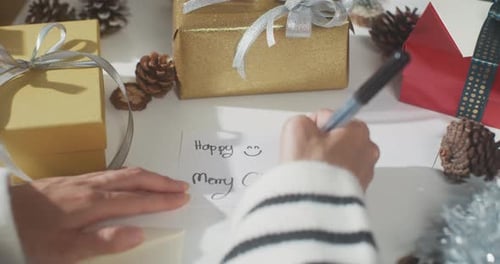 Close up of girl hands writing greeting card winter christmas decorations on table.