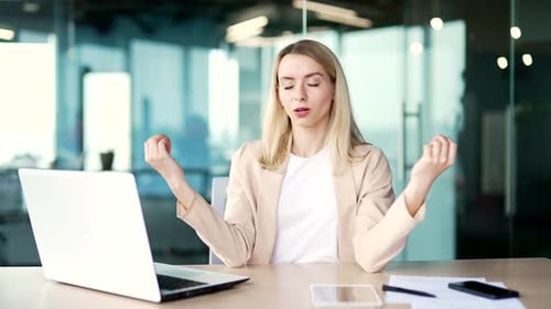 Young woman is meditating with her eyes closed while sitting at a workplace in the office.