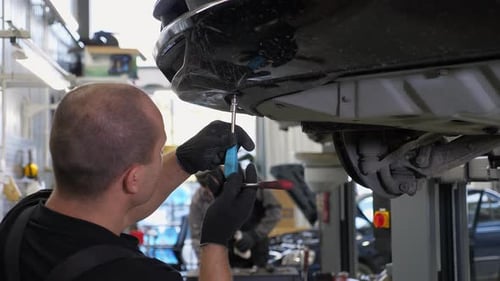 An Auto Mechanic Working Under the Car on a Car Lift in the Garage Car Service