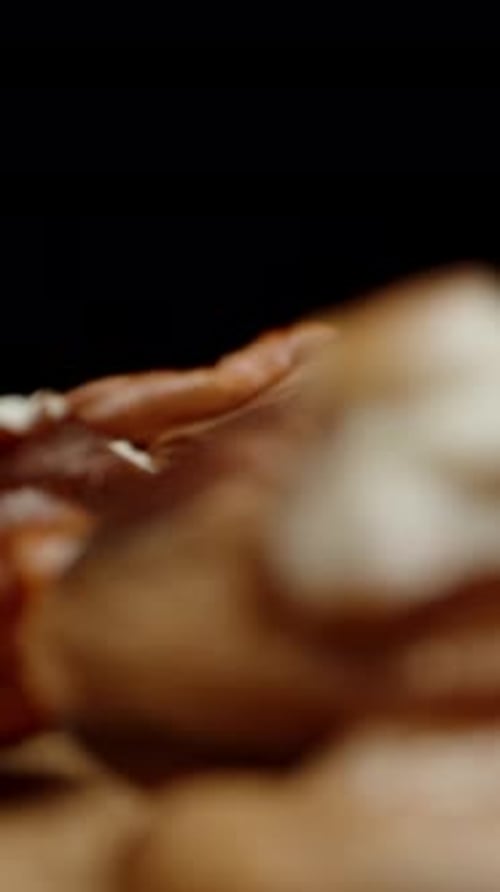 Vertical video. Peeled pecan nuts fall onto the table against a black background, close-up, slowed.
