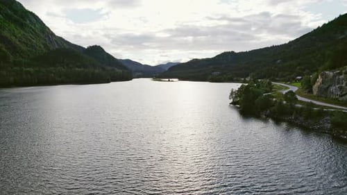 River Surrounded By Green Mountains And A Road On The Side