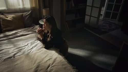 Woman kneeling on bed praying with rosary beads