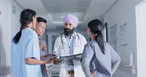 Diverse doctors and nurses using tablet and talking in corridor at hospital, in slow motion