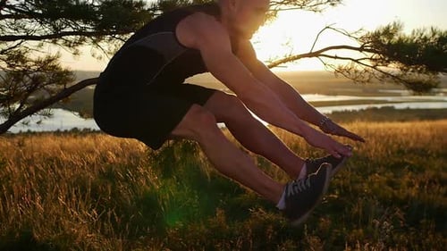 A Muscular Man in Sportswear Training on the Hill Jumping and Touching His Shoes with His Fingers