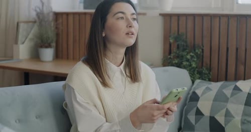Cheerful Young Lady Using Smartphone Thinking Then Texting and Smiling Enjoying Online Communication