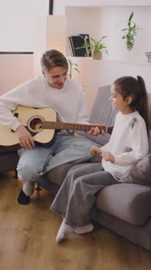 Man playing guitar with little girl inside house
