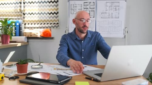 Architect Working on Blueprints at Desk in Office