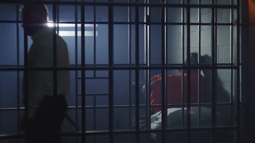 Prisoner Sits on the Bed in Prison Cell Jailer Walks the Corridor
