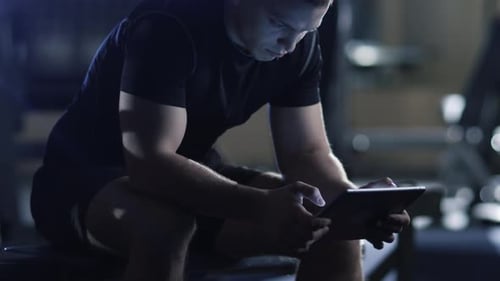 Handsome fit sporty man is using a tablet computer in the gym.