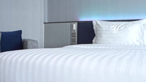 Double bed with white candid sheets and pillows in hotel room. Handheld