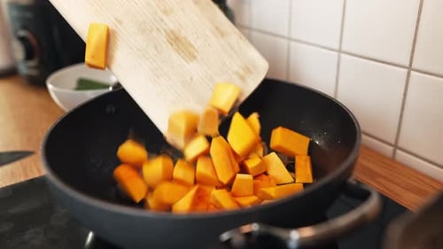 Nahaufnahme einer Person, die Mangostücke mit einem Holzlöffel in die Bratpfanne mit Zwiebelkuchen schiebt