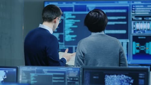 Na sala de controle do sistema, o especialista em TI e o engenheiro de projeto discutem enquanto seguram o laptop,