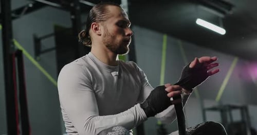 Fighter Puts on Hand Wraps While Sitting on the Edge of a Boxing Ring in a Musty Boxing Gym Camera