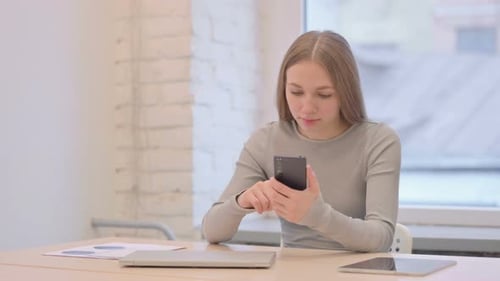Young Woman Using Smartphone at Desk Indoors