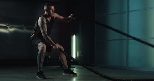 Tattooed Man Exercises with Battle Ropes in Gym