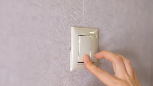 A luz está apagada, mão feminina, desliga um botão em uma parede cinza clara, vista frontal