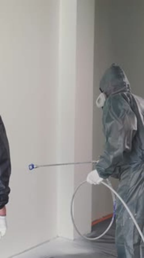 People Painting the Wall with Spray Gun Indoors