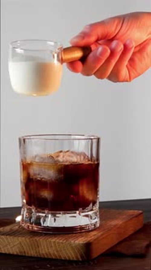 Pouring Milk into a Glass of Iced Coffee