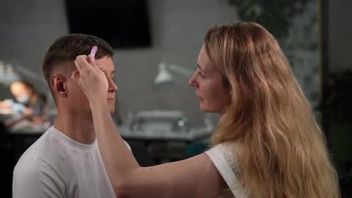 Beautician Carefully Shaping Eyebrows of Male Client Removing Hair with Hot Wax Demonstrating