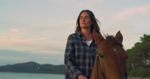 Low Angle Portrait of a Beautiful Woman Riding a Horse by on Seaside Beach at Sunset.