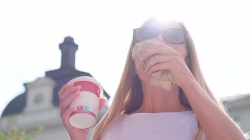 Woman Eating a Sandwich and Holding a Drink