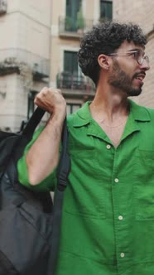 Brunette guy tourist with beard, dressed in green shirt, walks around city with backpack