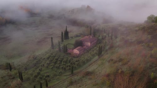 Mediterranean style farm building with cypress trees and morning mist, aerial