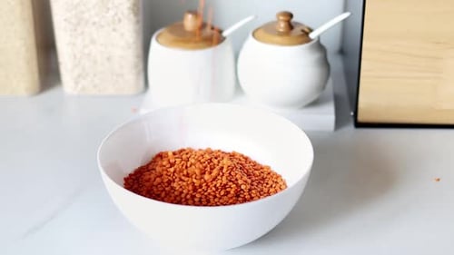 Red Lentils Being Poured Into White Bowl