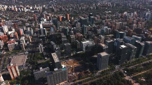 Aerial drone footage approaching a large urban park bordered by modern buildings under a clear blue