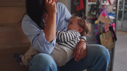 Mother sitting on stairs breastfeeding toddler in quiet home corner creating warm intimate moment