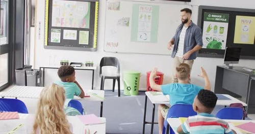 Diverse male teacher and happy schoolchildren at desk in school classroom