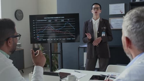 Physician Listening to Presentation and Taking Notes at Team Meeting in Office