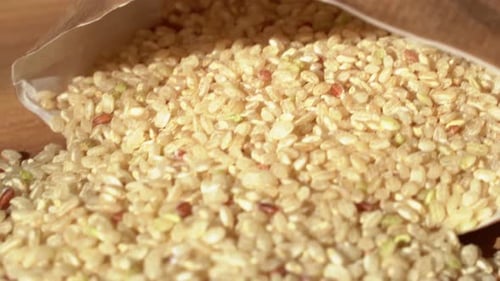 Slow movement backwards. Brown rice on a wooden table. Close up. Raw rice out of the paper bag.