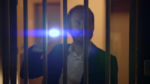 Man with Flashlight Behind Bars at Night
