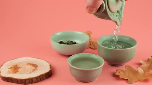 Warming up ceramic chawans with hot water from a gaiwan on the pink background. Slow motion.