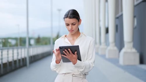Businesswoman sitting outside modern building walking working on tablet