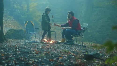 Smiling Family with Dog Sit Around a Campfire on Autumn Evening in the Woods Frying Sausages Over a