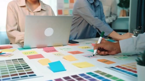 Collaborative Workspace with Laptop and Color Swatches as Team Members Discuss Creative Ideas and Pl