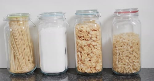 Close up of food storage jars with flour and various kinds of pasta on shelf in kitchen, slow motion