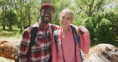 Portrait of happy diverse couple with backpacks embracing in park, slow motion