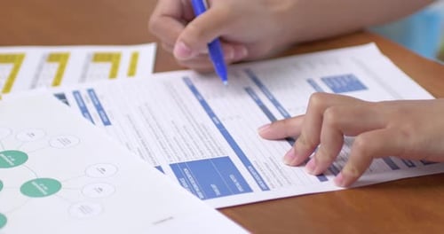 Student completing academic paperwork at desk classroom environment document focus overhead view