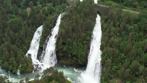 A beautiful waterfall flows from a steep mountain and flows into a large river. Aerial view. Norway.