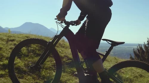 Close-up shot of a young athletic man on e-bike pedalling up the hill with a beautiful view.