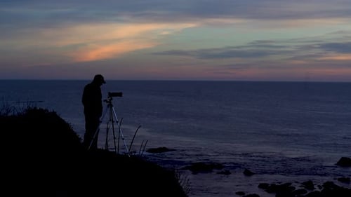 Silhouette eines Fotografen mit Blick auf den Ozean bei Sonnenuntergang