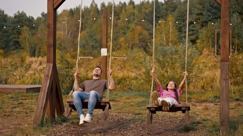 Loving couple man and girl riding on large wooden swing overlooking a beautiful lake in nature